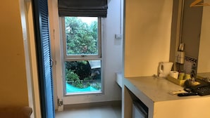 A small, clean bathroom with a toilet, sink, and a window overlooking a garden. - L42 Hostel (Bangkok)