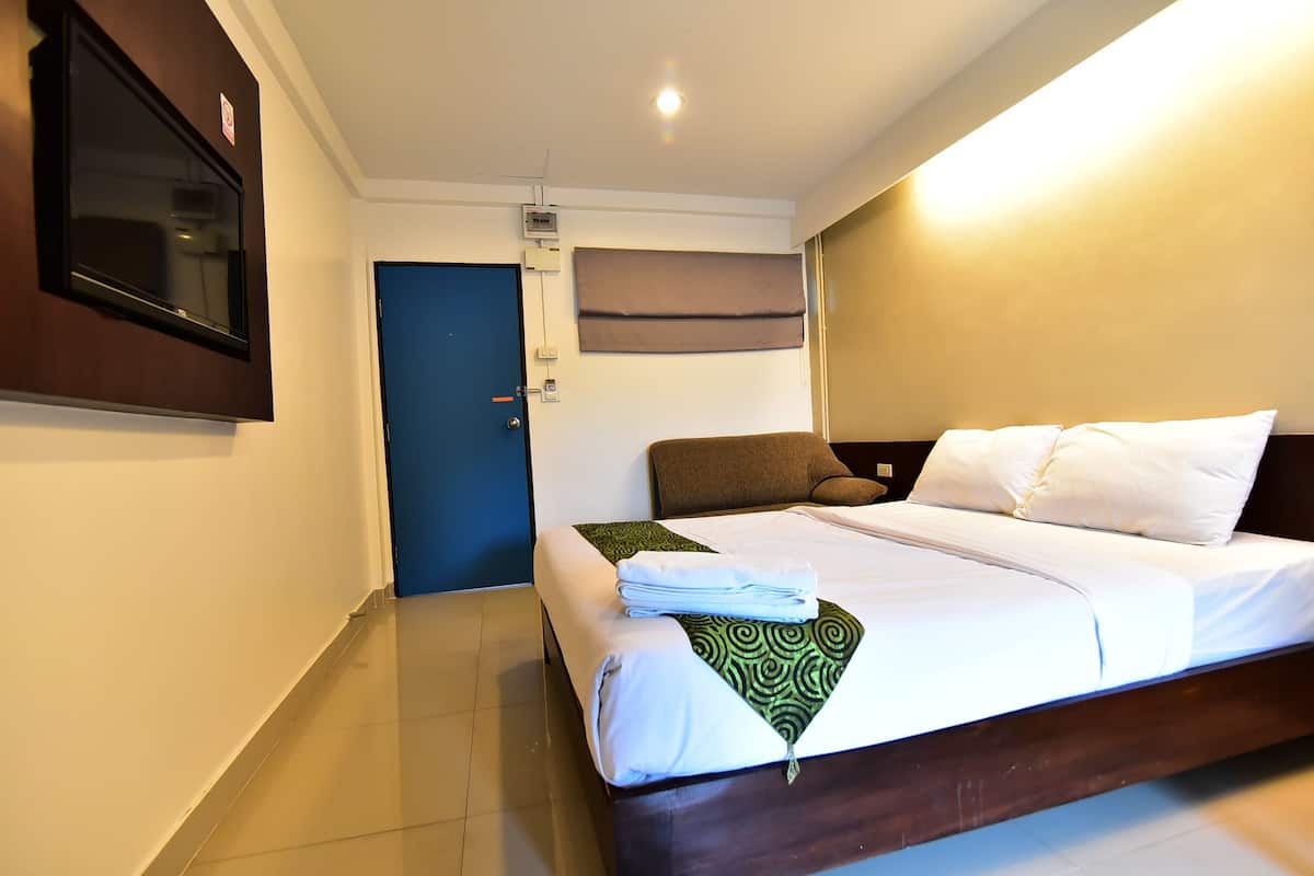 A hotel room with a bed, a TV mounted on the wall, a door, and a window with blinds.