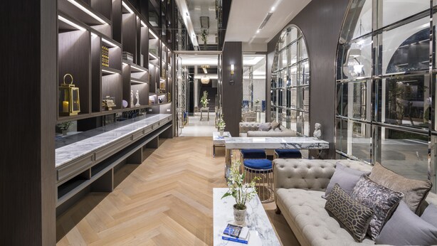 Een modern interieur met een centraal ziteiland, een lange presentatie van objecten op planken, en grote ramen die zorgen voor daglicht.