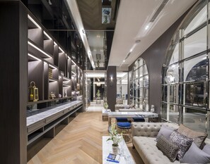Ein modernes Interieur mit einer zentralen Sitzgruppe, einer langen Vitrine mit Gegenständen und großen Fenstern, die natürliches Licht hereinlassen.