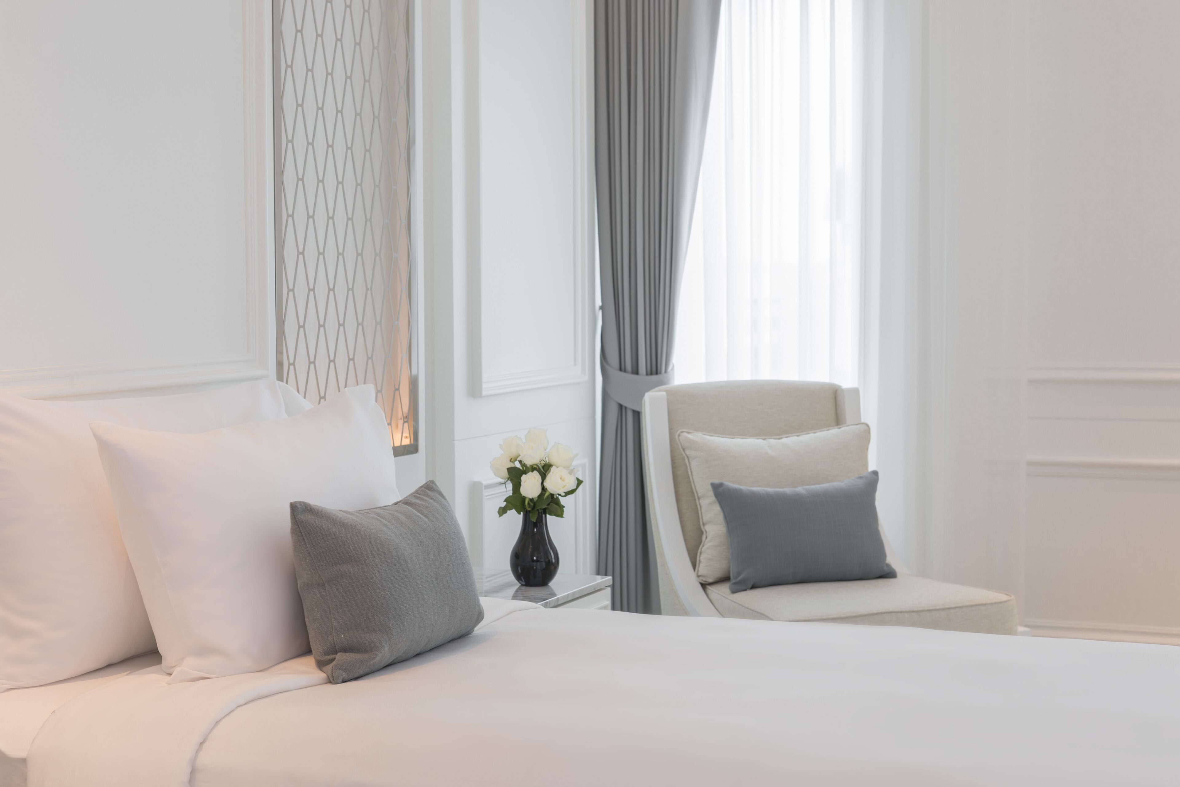 Un dormitorio ordenado con una cama, una silla y un jarrón con flores.