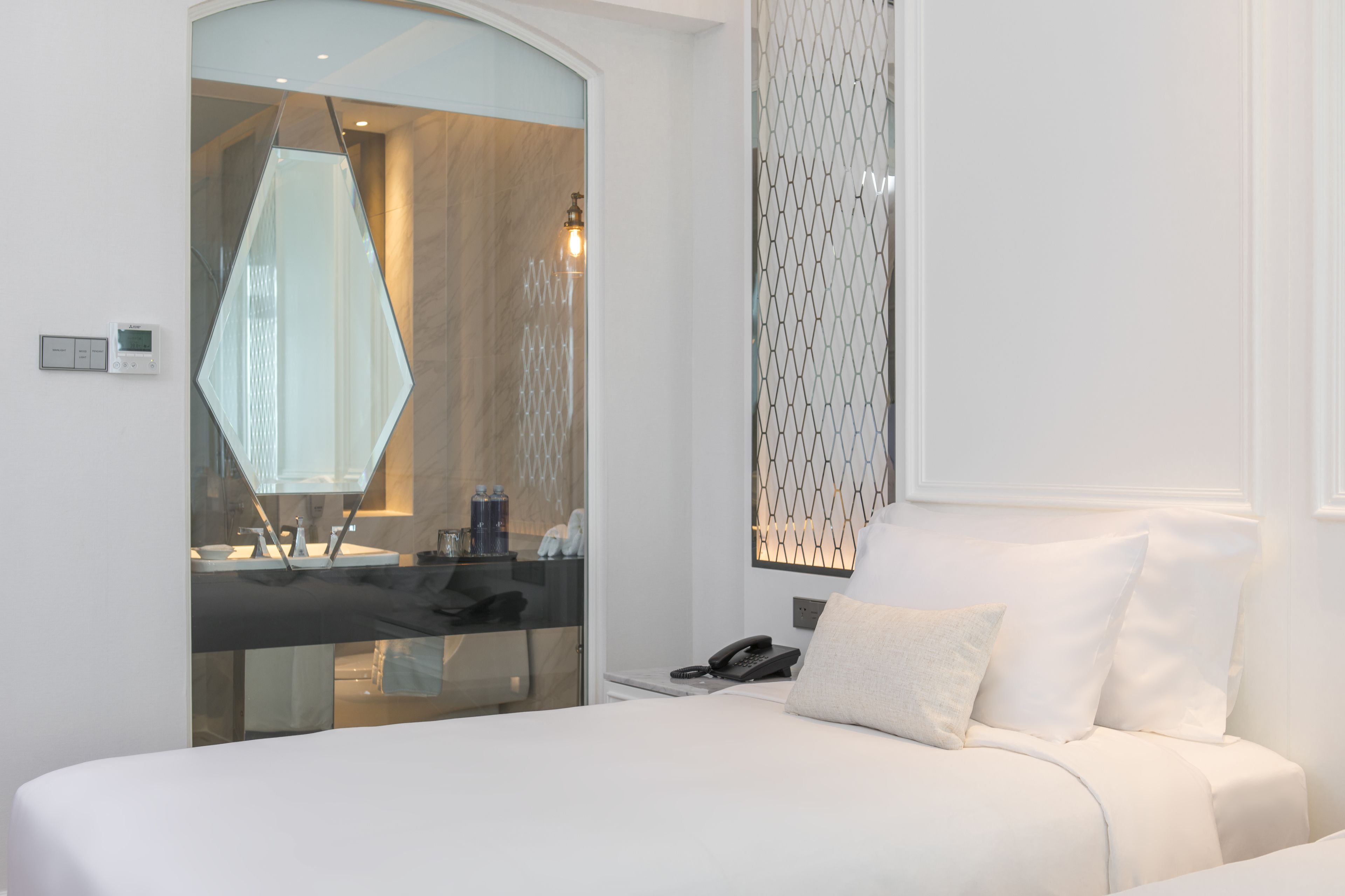 Una habitación de hotel moderna con una cama grande, un baño con paredes de vidrio y un panel decorativo en la pared.
