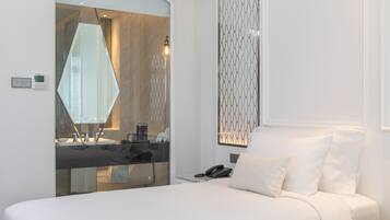 Una habitación de hotel moderna con una cama grande, un baño con paredes de vidrio y un panel decorativo en la pared.