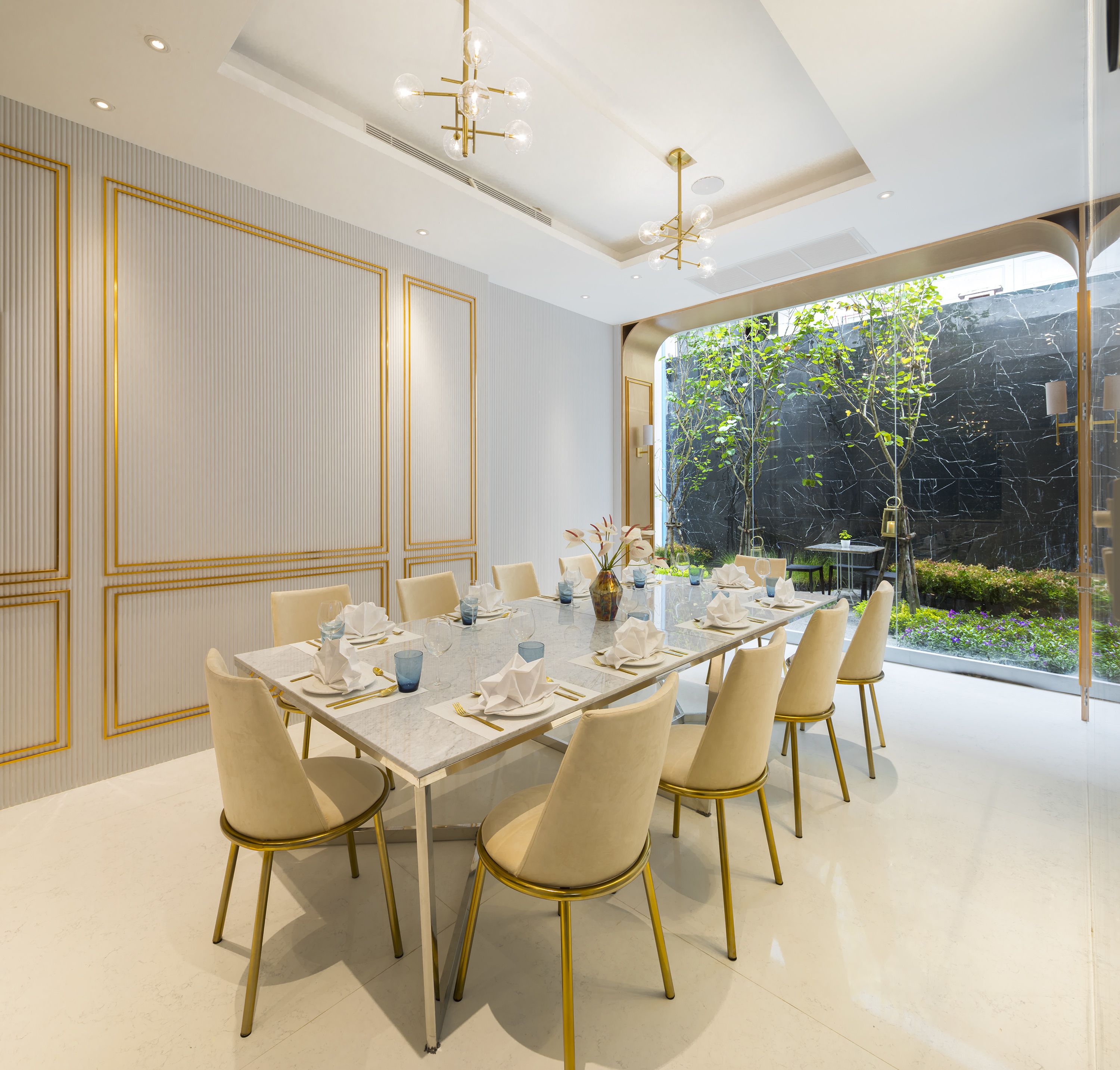 Ein moderner Speisesaal mit einem langen Tisch, goldenen Stühlen und einer Chandelier.