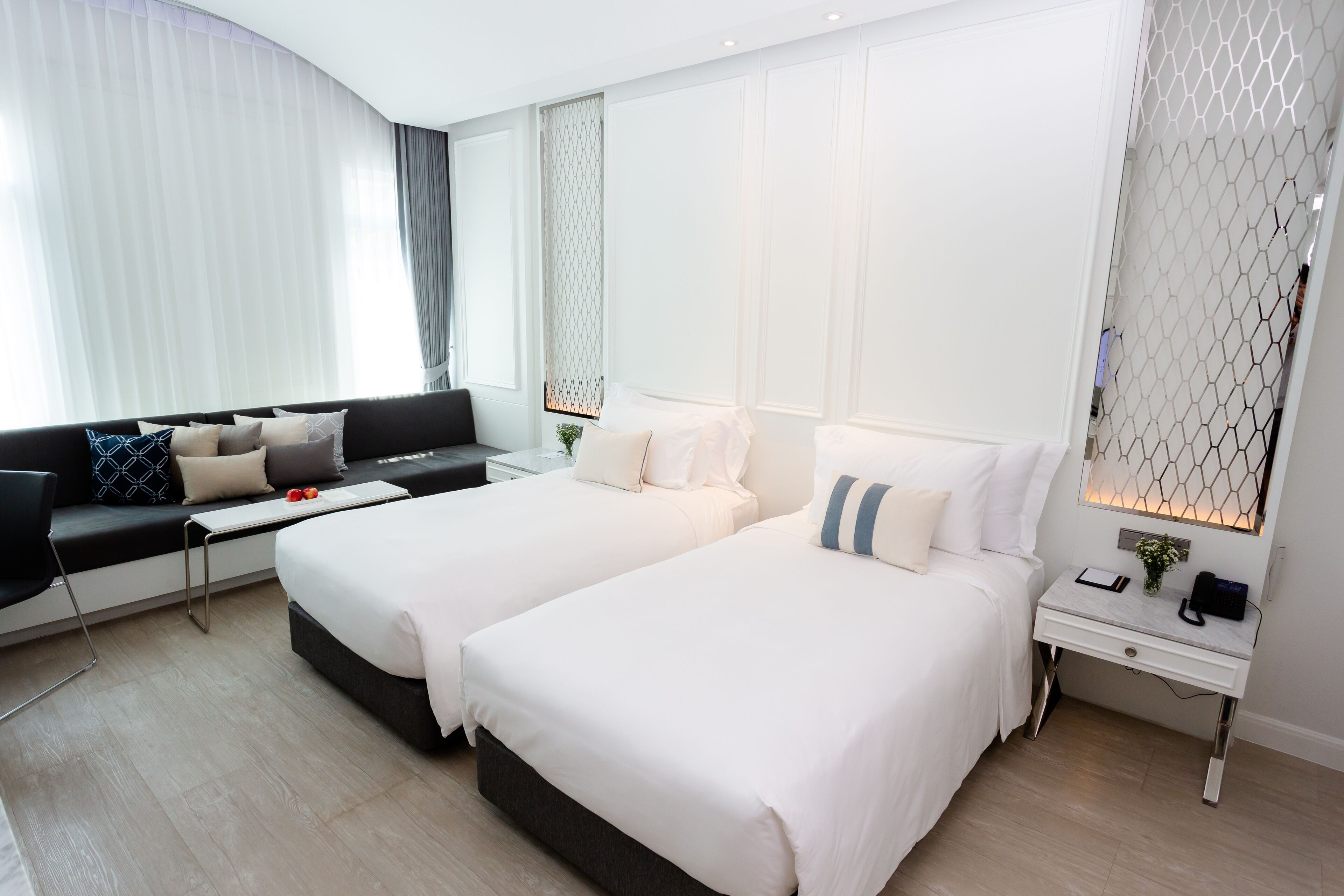 Una habitación de hotel moderna con dos camas, un sofá, una mesita y una mesita de noche.