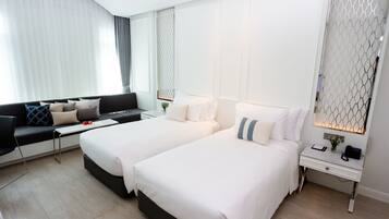 Una habitación de hotel moderna con dos camas, un sofá, una mesita y una mesita de noche.