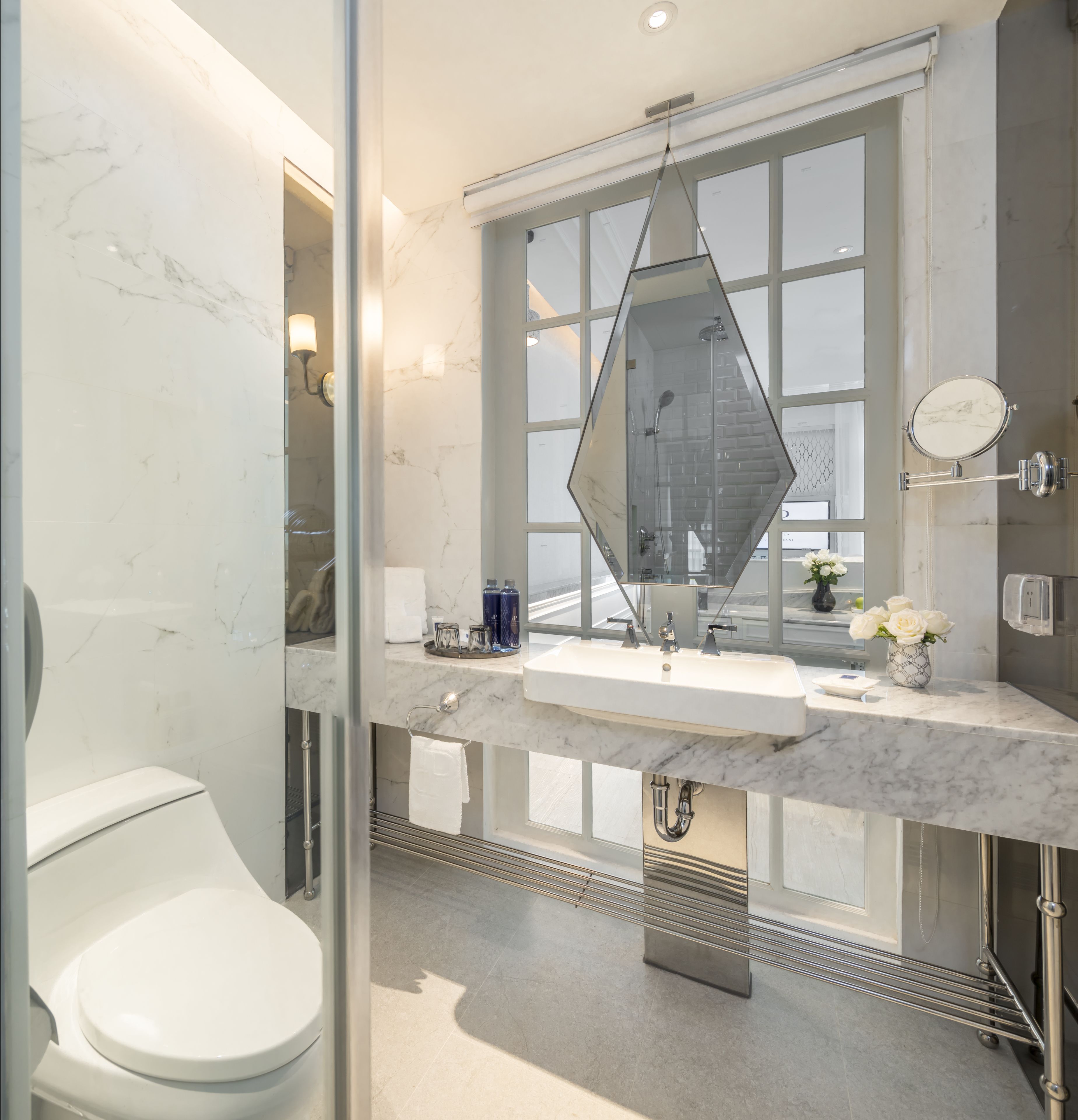 A modern bathroom with a large window, a geometric mirror, and a marble countertop.