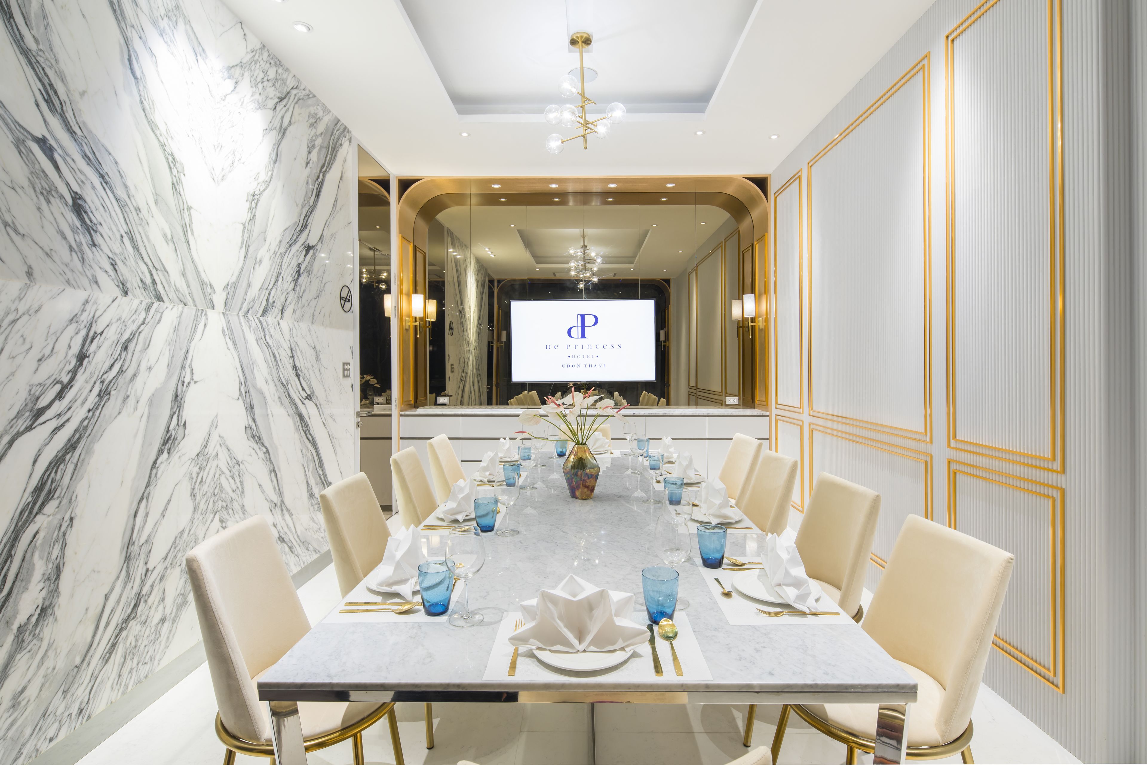 Un salón de conferencias con una mesa de mármol, sillas blancas y una pantalla grande que muestra un logotipo.