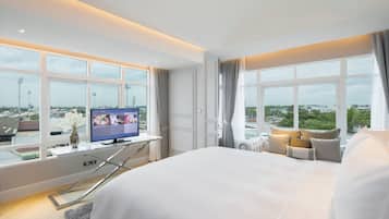 Habitación de hotel moderna con una cama grande, un escritorio con una computadora y vistas a la ciudad a través de amplios ventanales.
