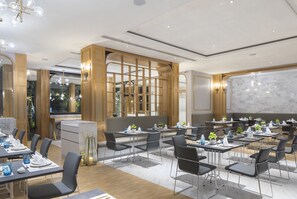 A modern dining area with tables and chairs, a marble wall, and a large window. - De Princess Hotel Udonthani (Udon Thani)