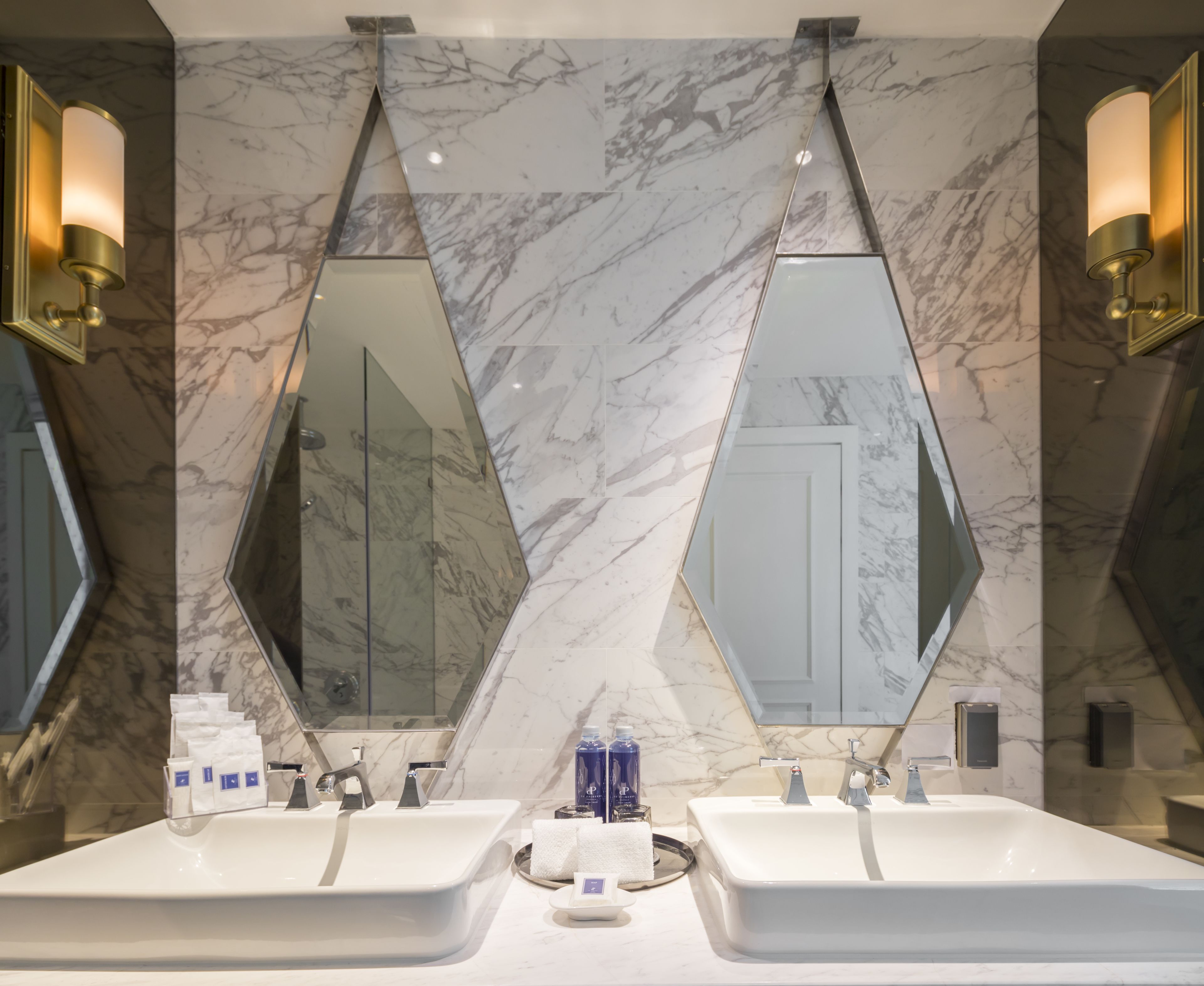 Un bagno con due lavabi, pareti in marmo e luci a parete.