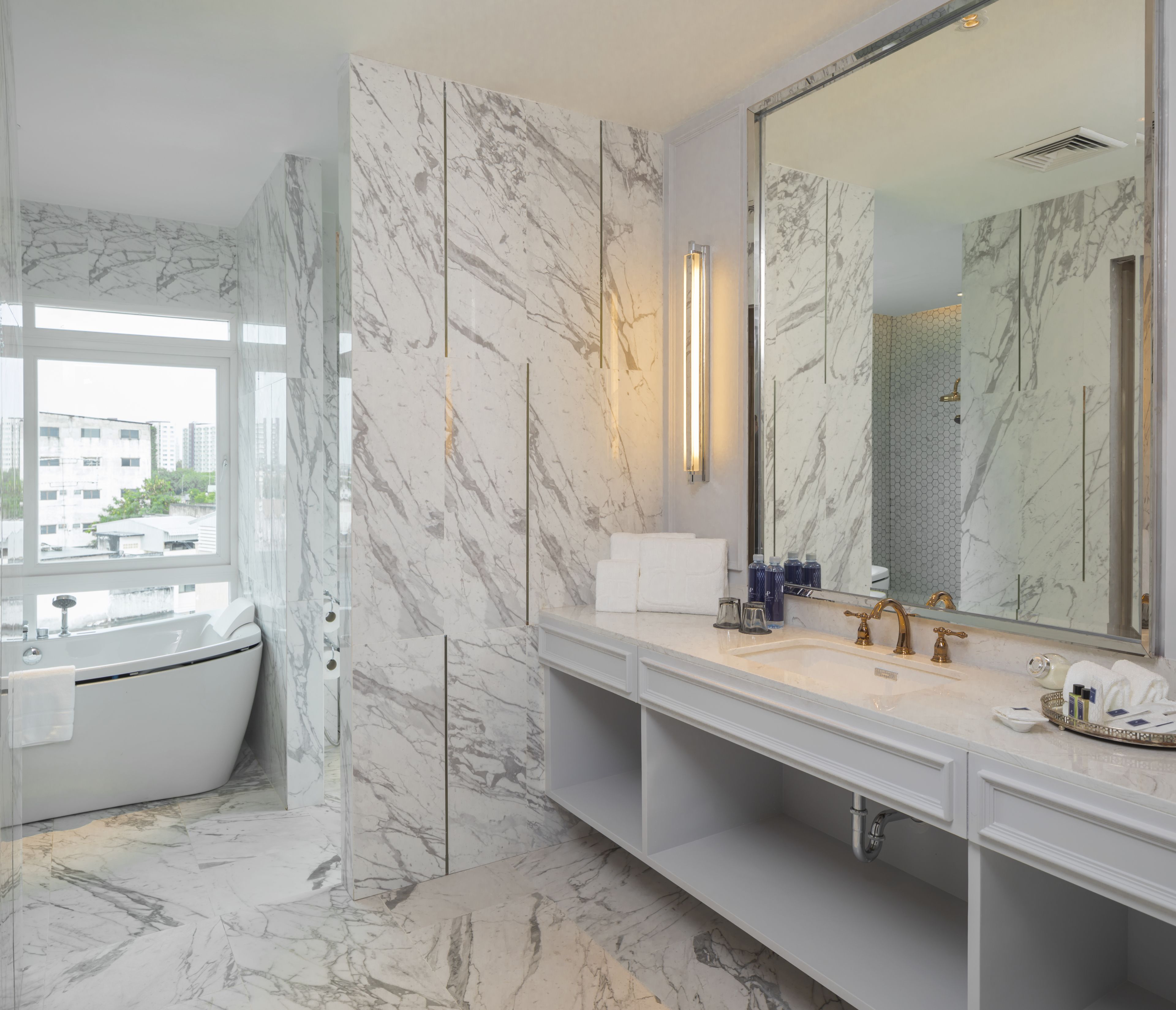 Une salle de bain moderne avec une baignoire sur pieds, un grand miroir et des murs en marbre.