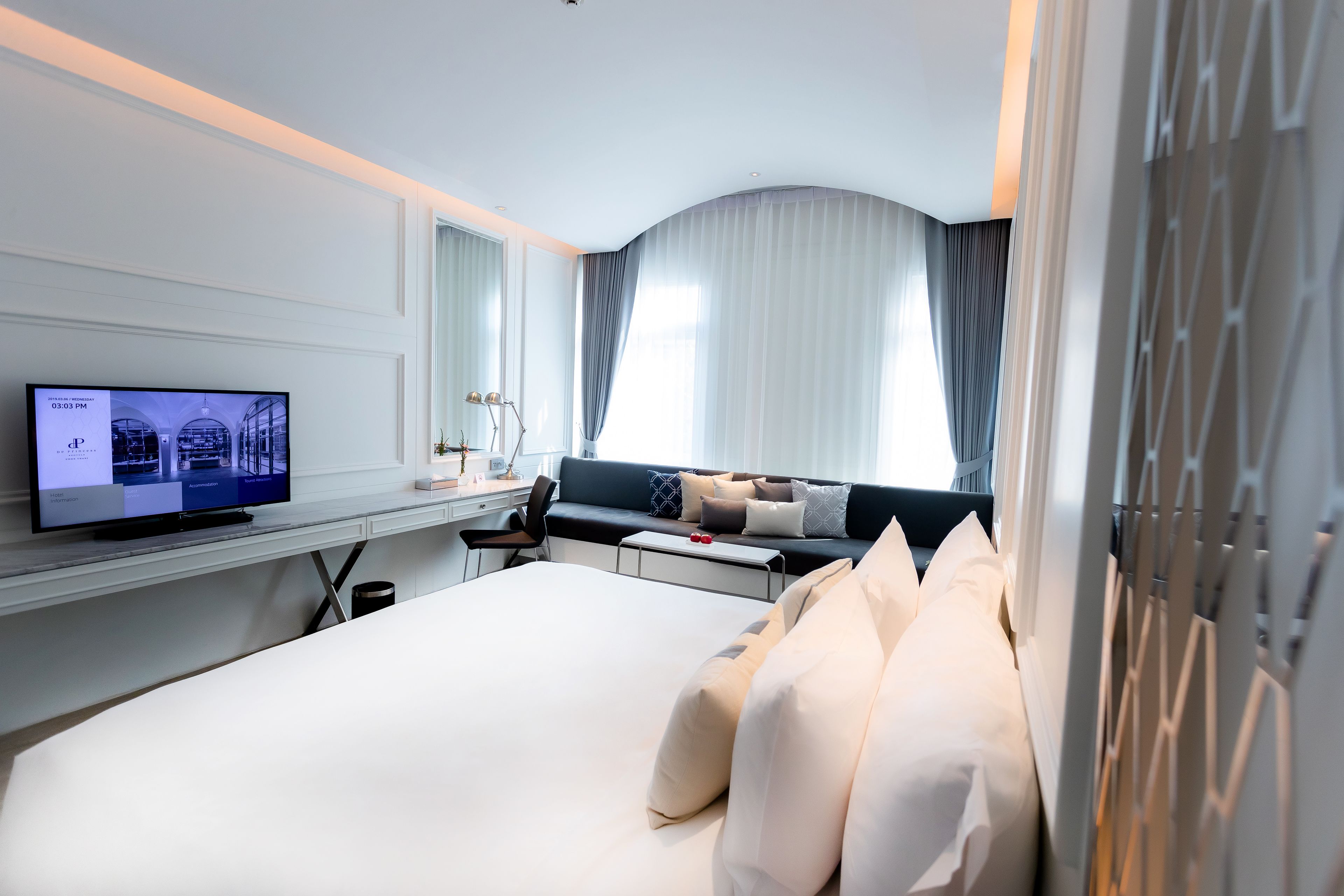 Une chambre d’hôtel moderne dotée d’un grand lit, d’un bureau avec un ordinateur, d’une télévision et d’une fenêtre avec des rideaux.
