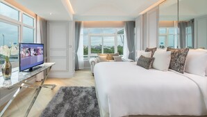 Een moderne hotelkamer met een groot bed, een televisie op een marmeren console, uitzicht op de stad door grote ramen en een gezellige zithoek.