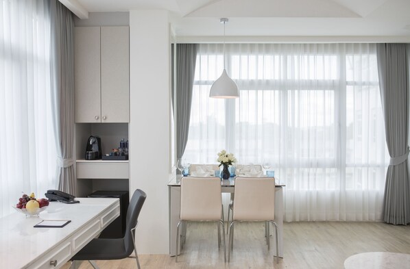 A modern hotel room with a dining area, a desk with a telephone, a bowl of fruit, and a vase of flowers. - De Princess Hotel Udonthani (Udon Thani)
