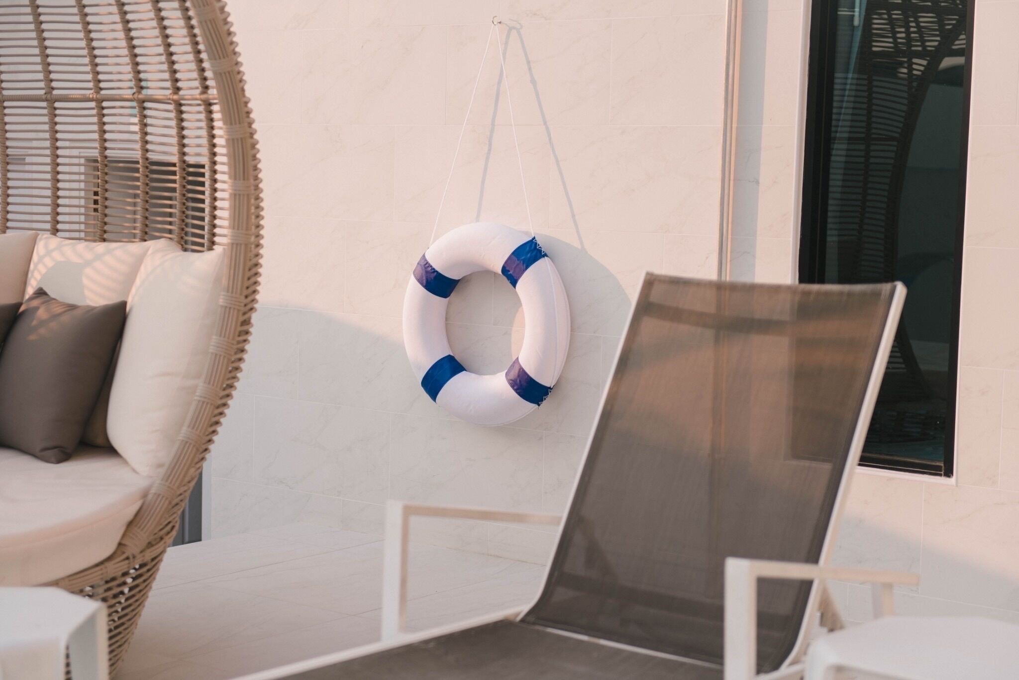 A wicker lounge chair with cushions, a white armchair, and a life ring hanging on the wall.