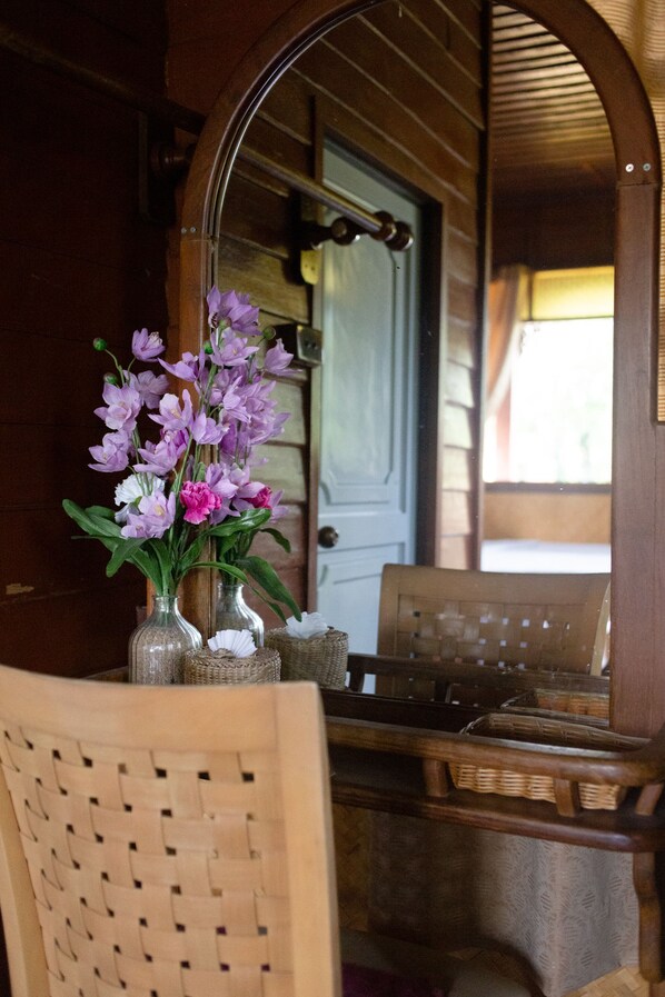 A wooden interior with a mirror reflecting a door, a wicker chair, and a table with a vase of flowers.