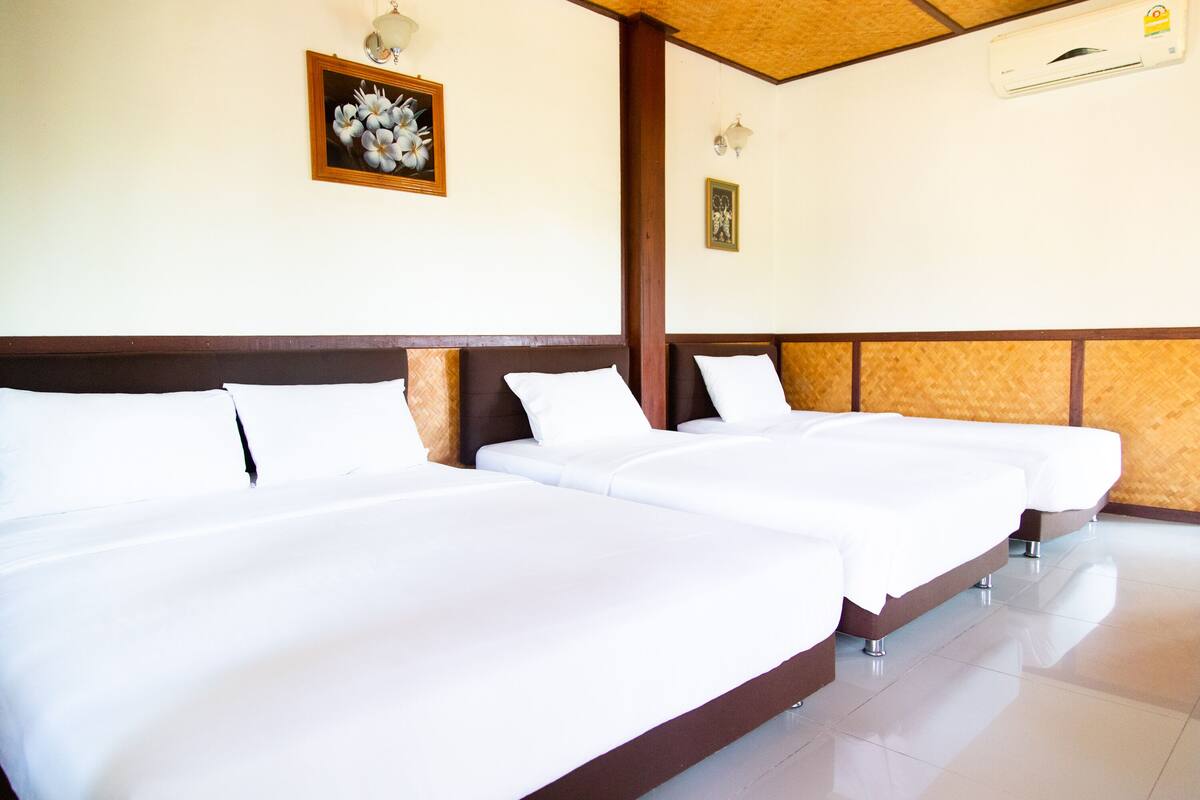 Habitación de hotel con tres camas individuales, un cabecero de madera, una obra de arte floral enmarco y un aire acondicionado de pared.