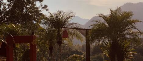 A pathway leading to a red archway surrounded by lush greenery and palm trees, with a mountainous backdrop.