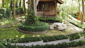 A wooden cabin surrounded by a well-maintained garden with stone pathways and neatly trimmed hedges. - Baanpufa Resort (Sai Yok)