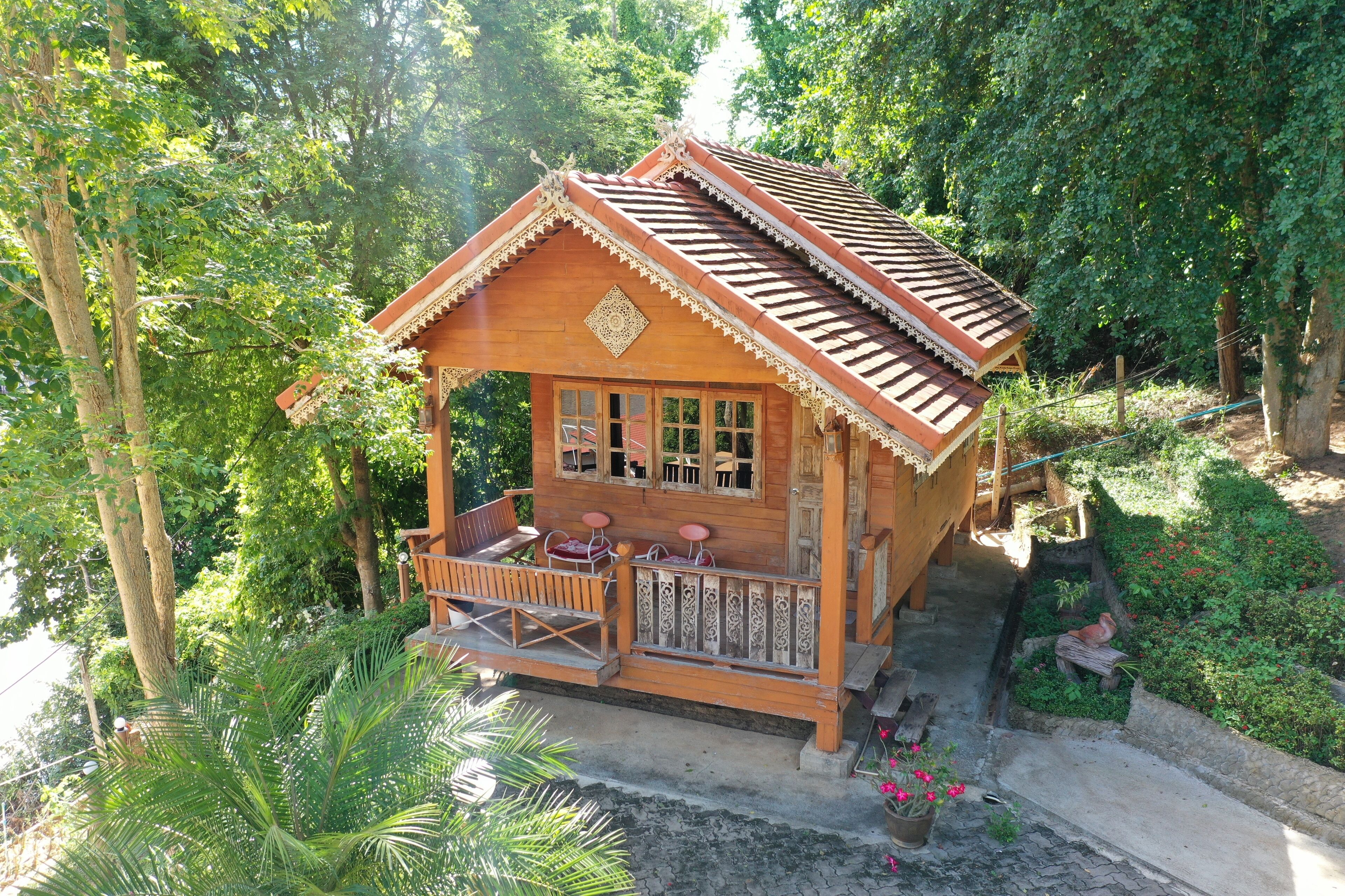 A wooden house with a balcony, surrounded by lush greenery.