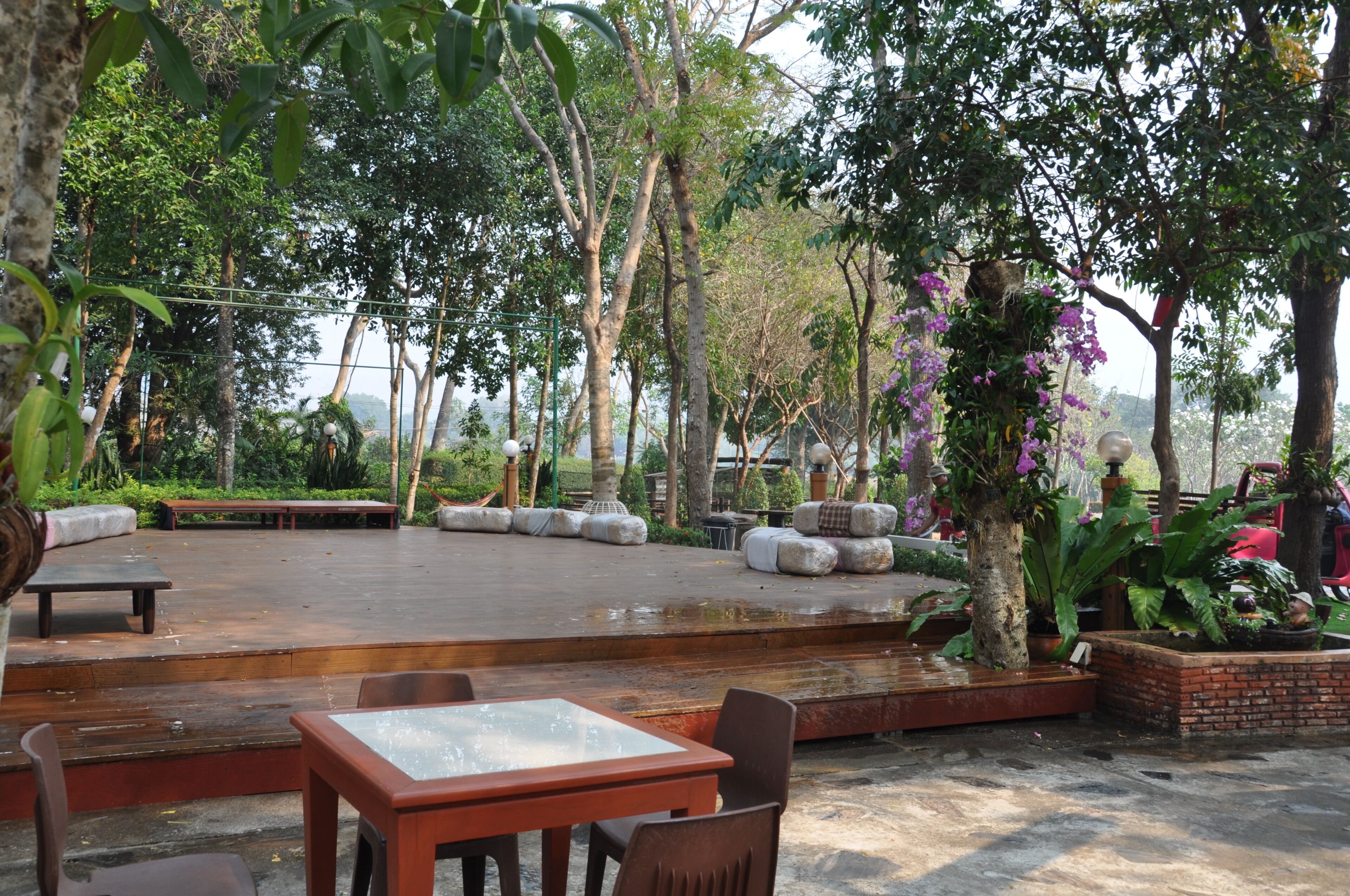 An outdoor seating area with tables and chairs, surrounded by lush greenery and trees.