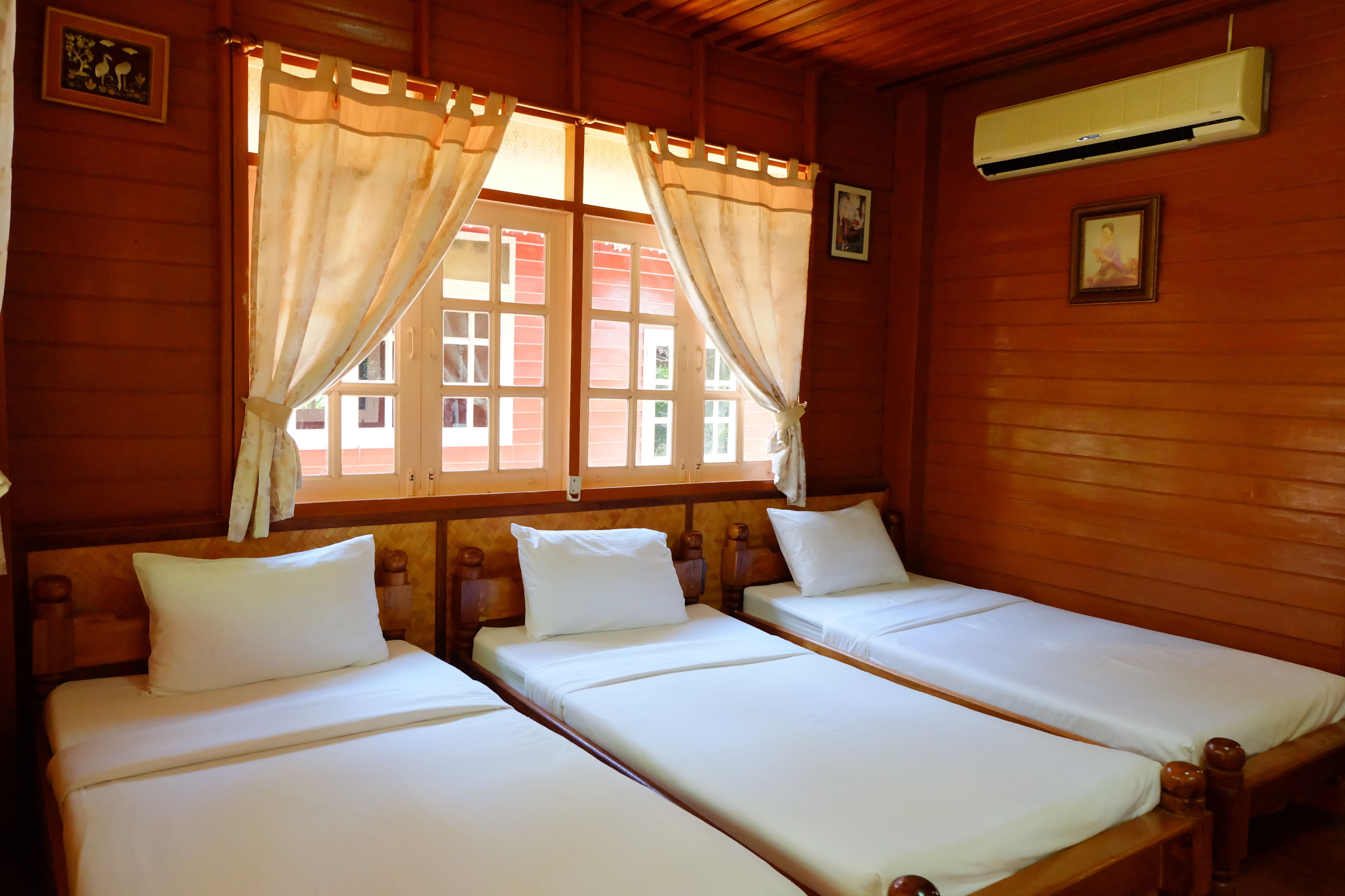 Ein Zimmer mit drei Holzbett, weißer Bettwäsche und einem Fenster mit Vorhängen.