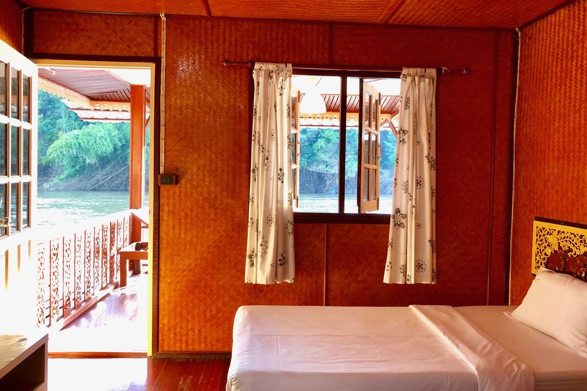 Una habitación con cama, ventana con cortinas y vista al río.
