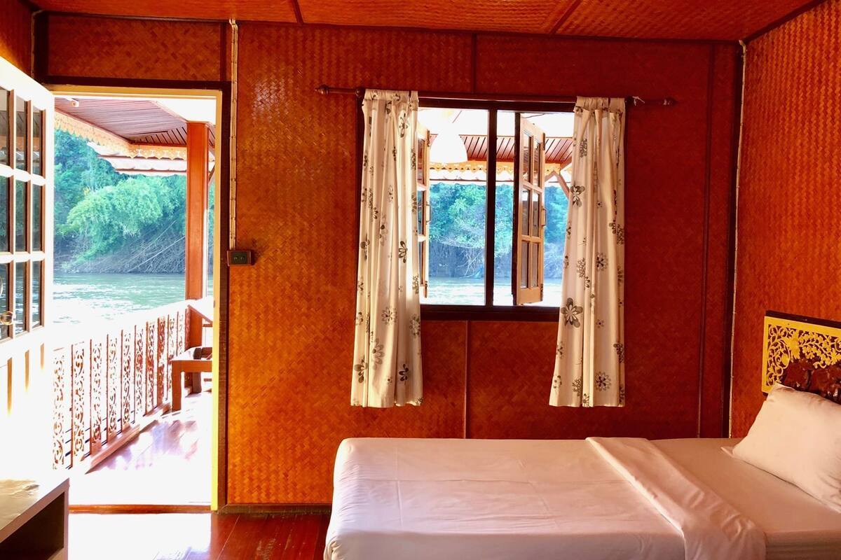 Una habitación con una cama, un ventanal con cortinas y vista a un río.