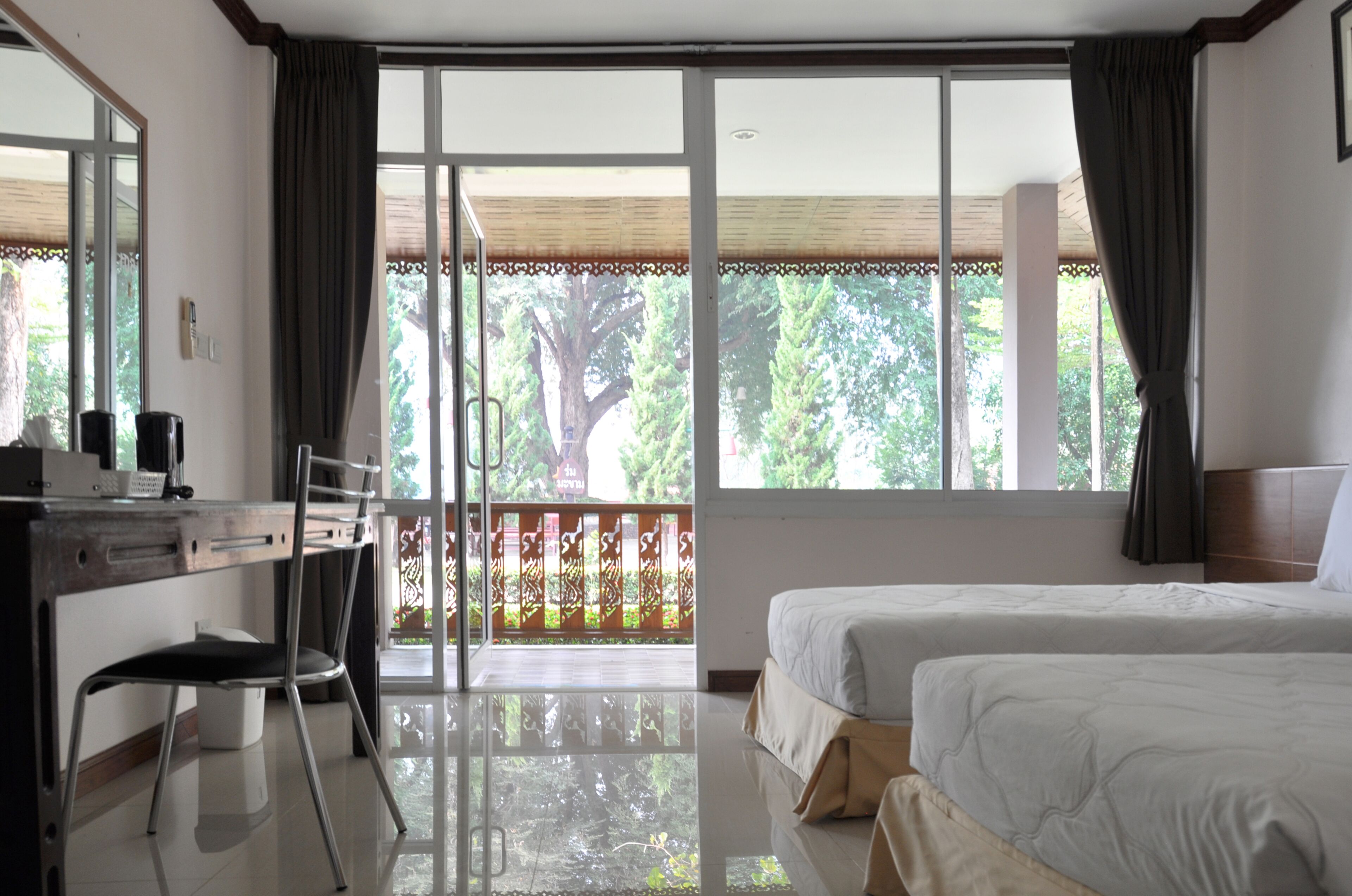 A hotel room with a desk, two beds, and a balcony with a view of trees.