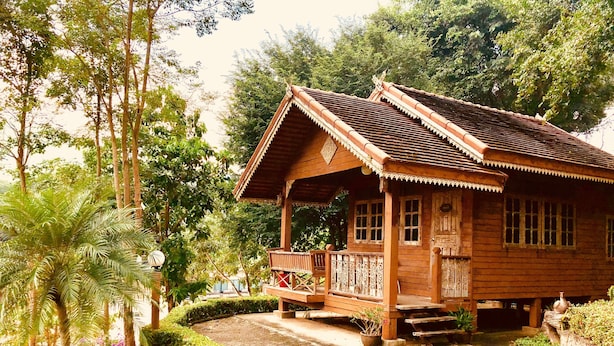A wooden house with a porch, surrounded by lush greenery and trees. - Baanpufa Resort (Sai Yok)