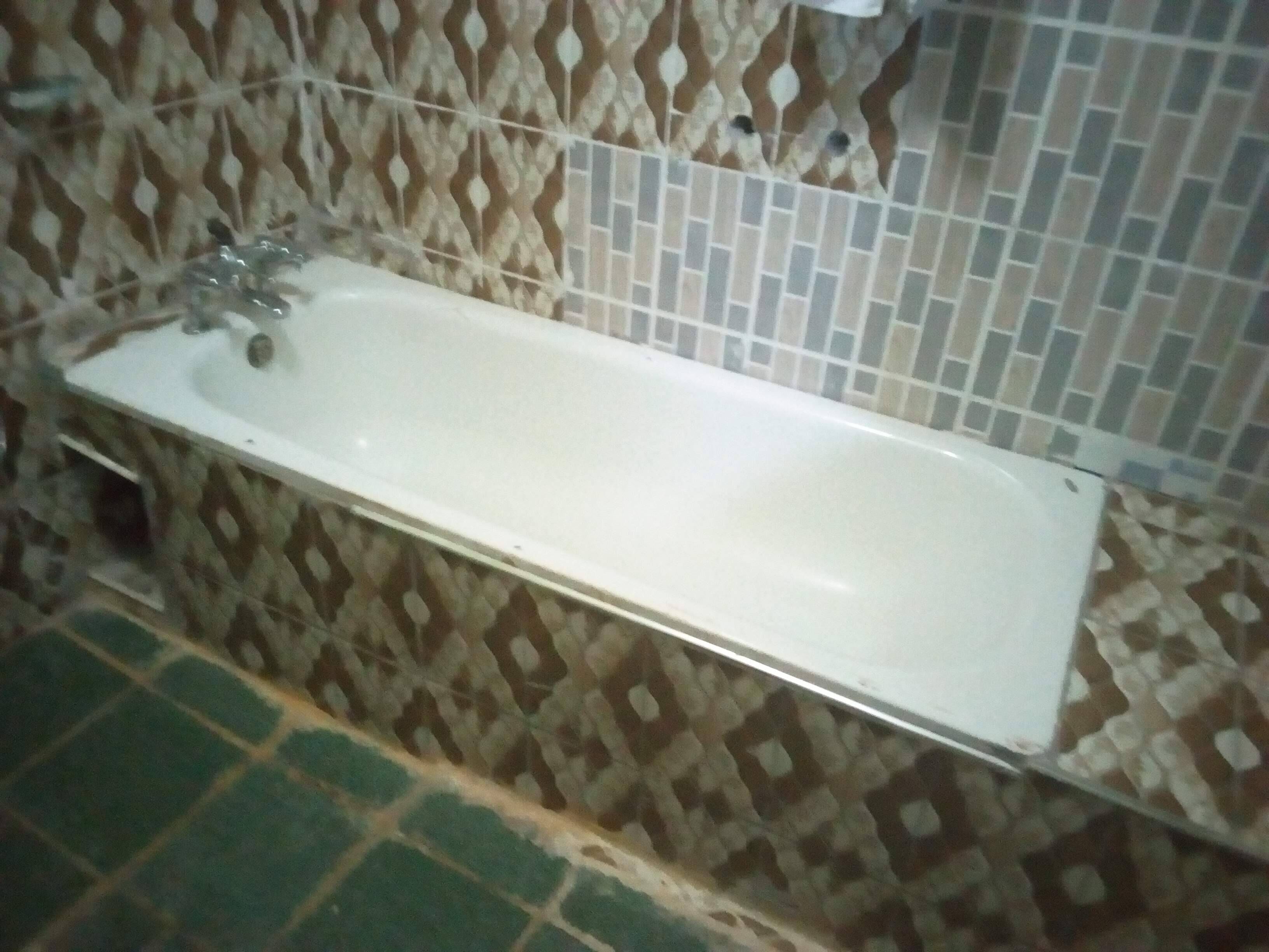Un baño con una bañera blanca, azulejos decorados en las paredes y un suelo de baldosas verdes.