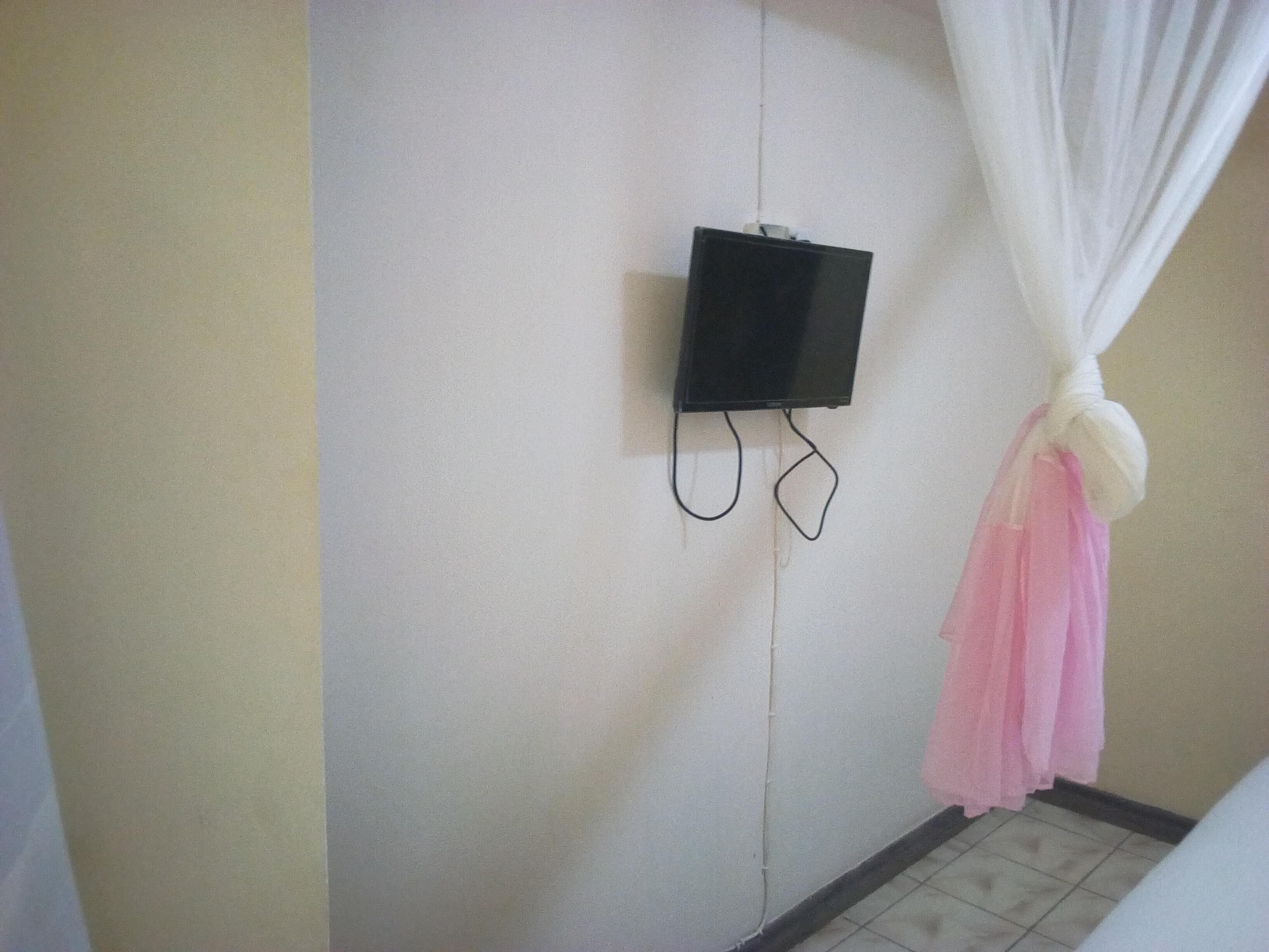 Ein Zimmer mit einem an der Wand befestigten Fernseher, einem Vorhang und einem gefliesten Boden.