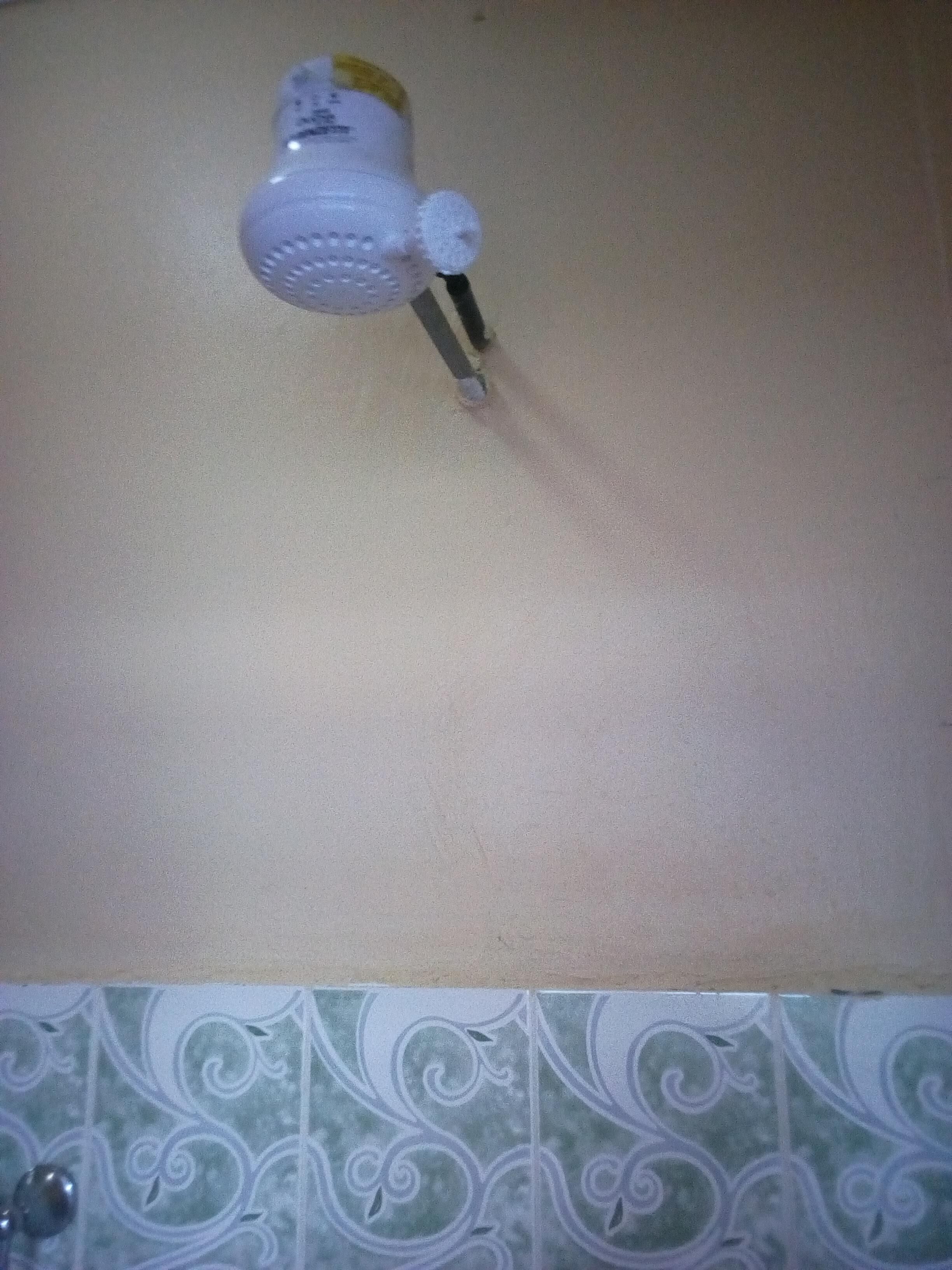Casa de banho com chuveiro branco fixado numa parede bege.