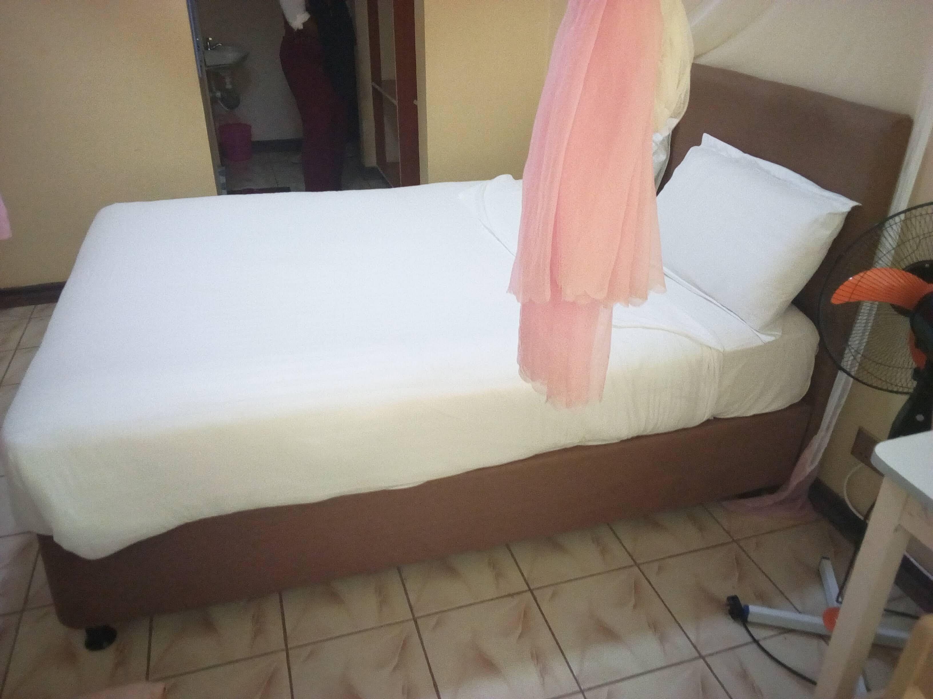 A single bed with a white mattress and a peach-colored blanket.