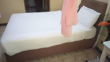 A single bed with a white mattress and a peach-colored blanket.
