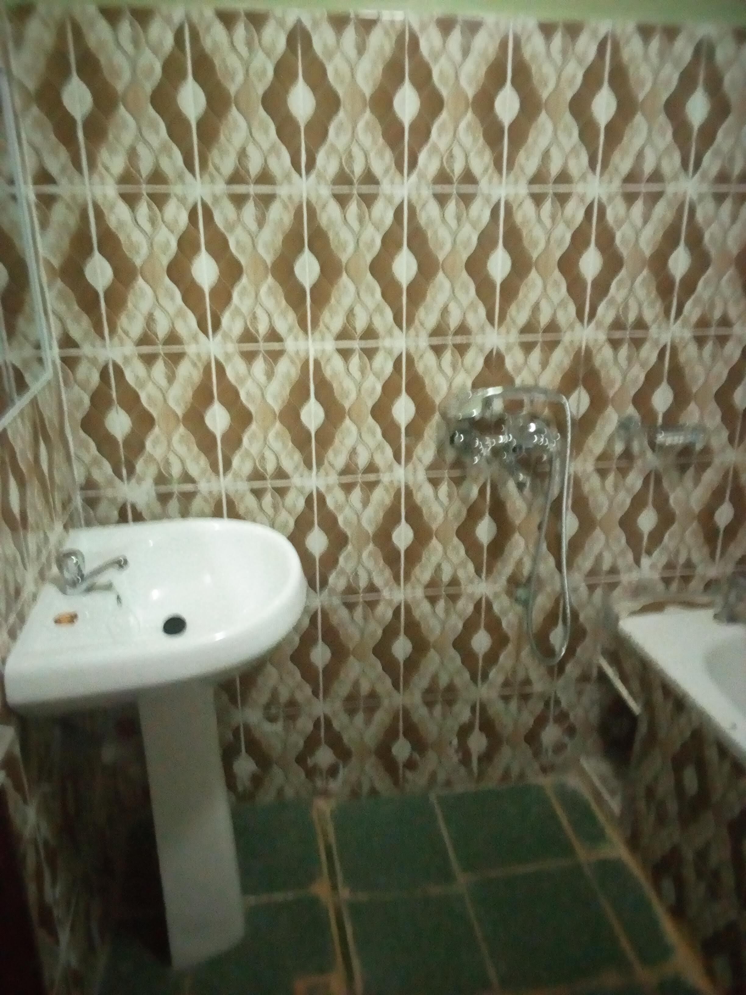 Un baño con pared de azulejos estampados, un lavamanos y un espejo.