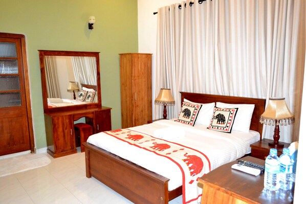 A hotel room with a wooden bed, bedside lamps, a nightstand with a remote control, and a mirror. - Capital Regency Hotel (Kandy)