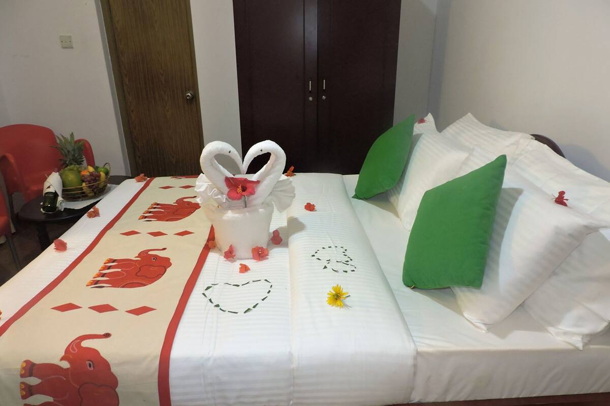 A hotel room with a bed, a red chair, a fruit basket, and a wooden door.