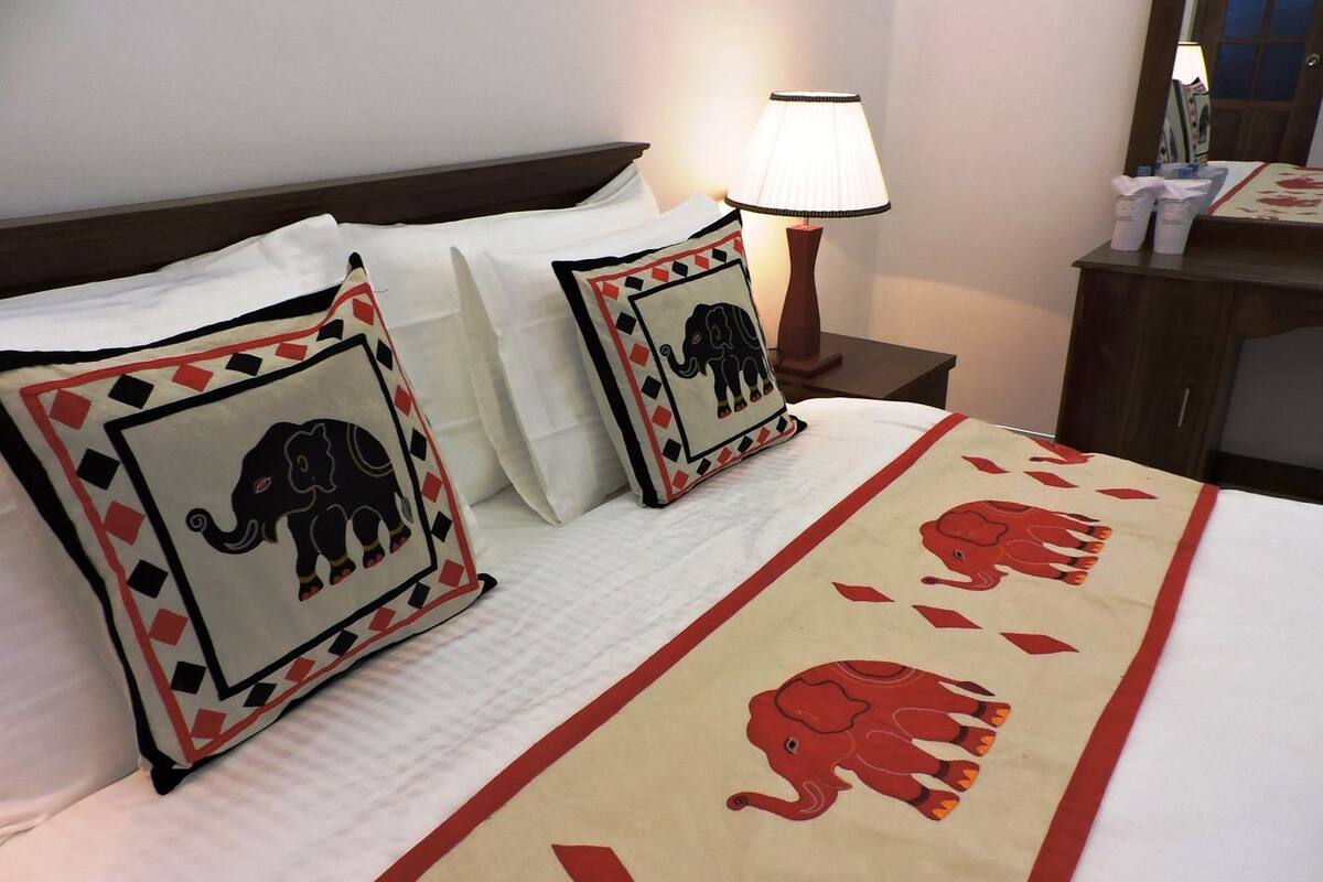 A hotel room with a bed, two pillows with elephant designs, a bedside lamp, and a nightstand with toiletries.