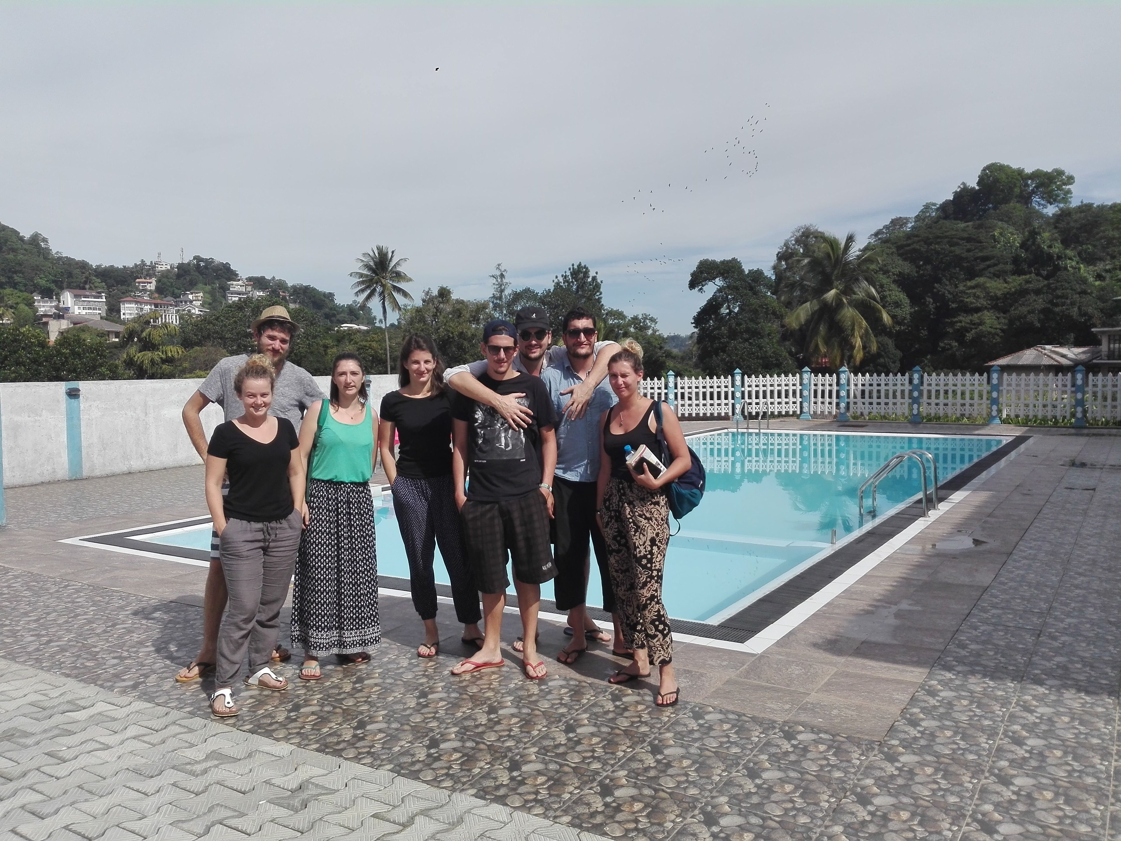 A group of people standing by a swimming pool with a white picket fence in the background.
