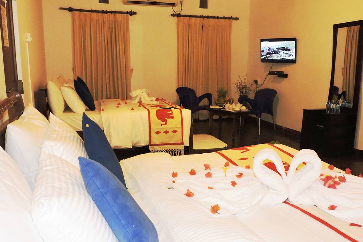 A hotel room with two beds, a TV, a desk with chairs, and a dining table.