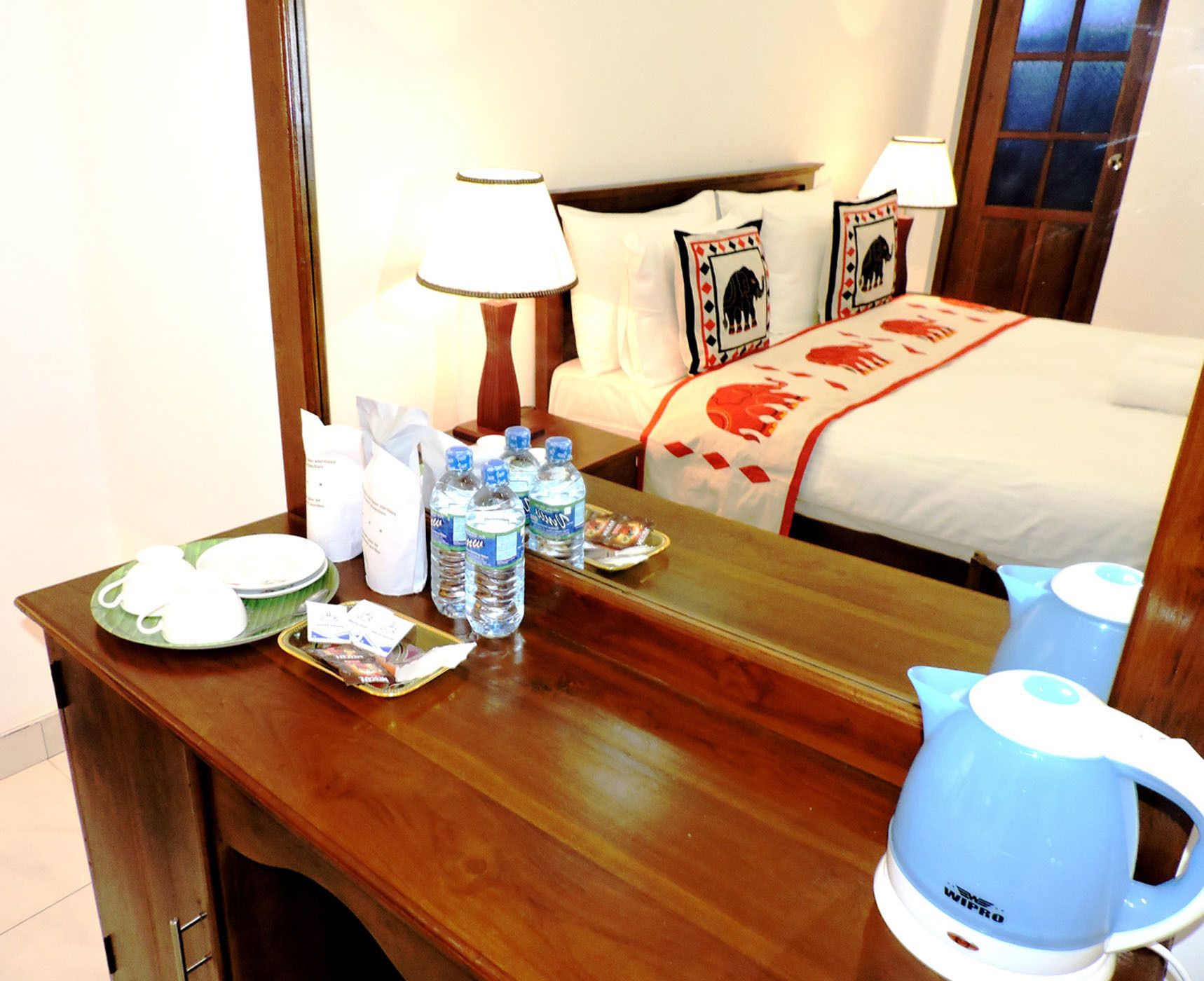Une chambre d’hôtel avec un bureau en bois, un lit recouvert d’une courtepointe à motifs de buffles et une bouilloire bleue posée sur la table.