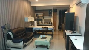 Un espacio habitable compacto con sofá, una mesita, televisor y una kitchenette al fondo.