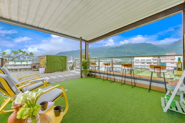 A rooftop terrace with green artificial grass, yellow lounge chairs, and a view of mountains and buildings. - Tian Yan Mountains (Jiaoxi)