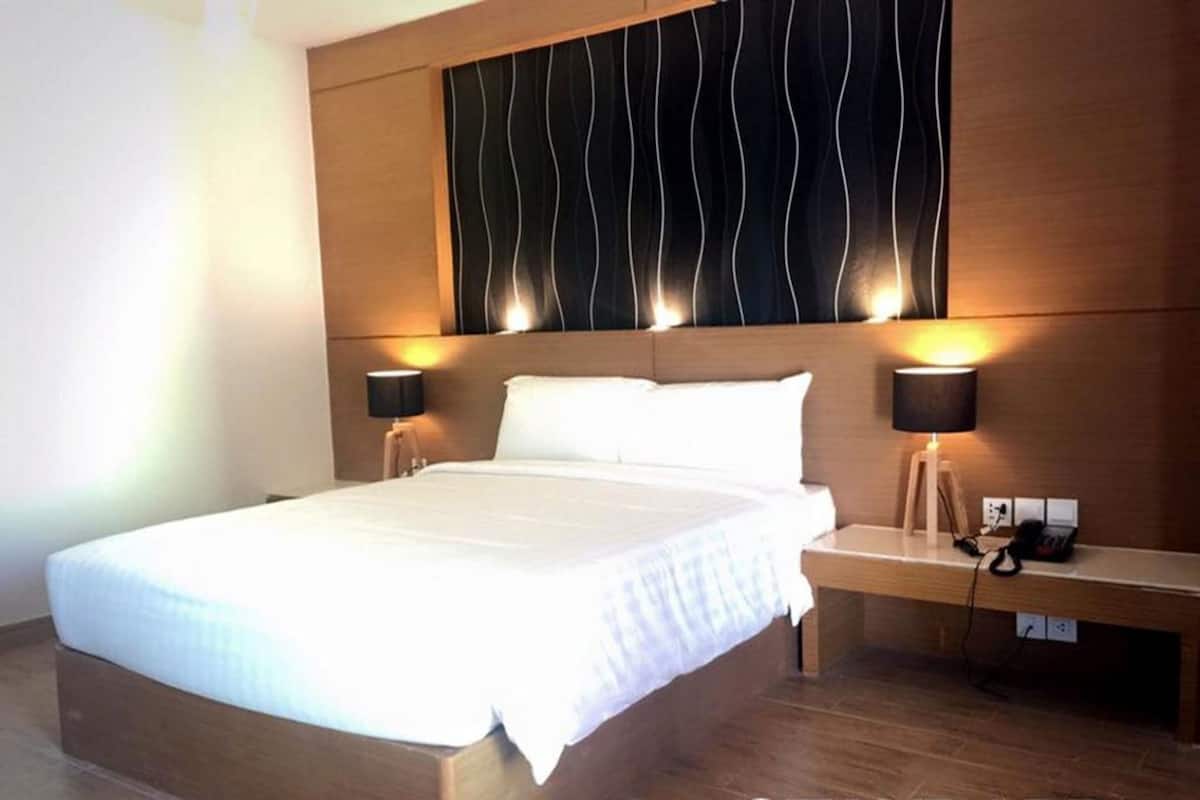 A hotel room with a large bed, bedside lamps, a wooden headboard, and a nightstand with a phone and charger.