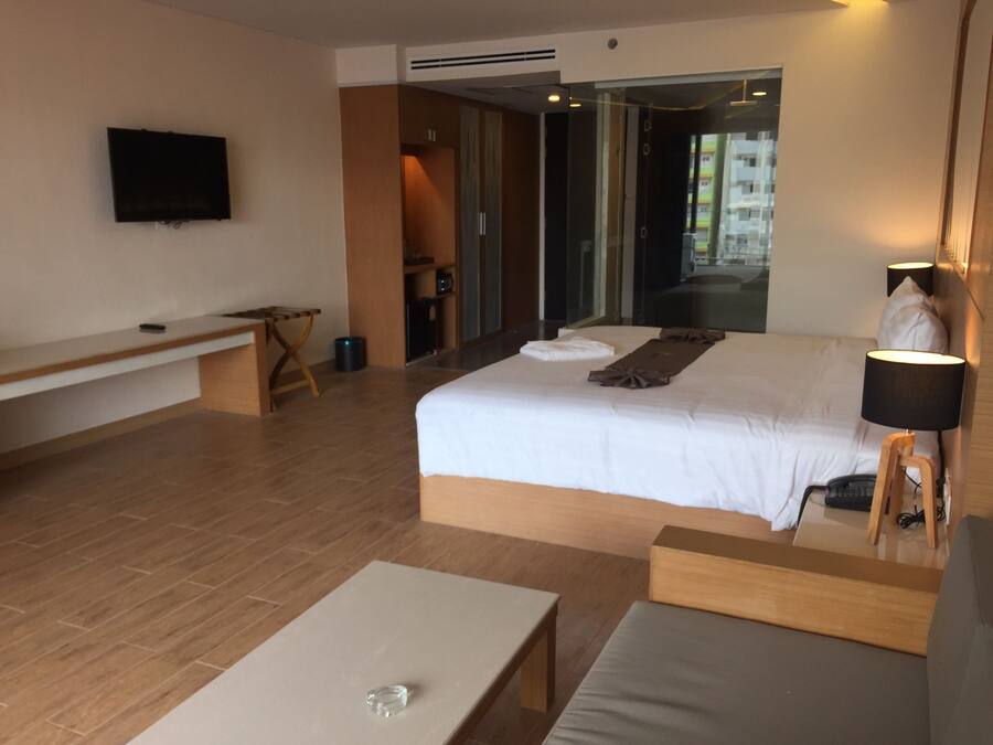 A modern hotel room with a large bed, a bedside table, a desk, a chair, and a TV mounted on the wall.
