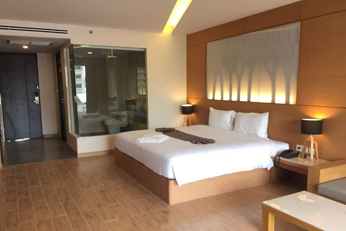 A modern hotel room with a large bed, bedside tables with lamps, a wooden headboard, and a large window with a view of trees.