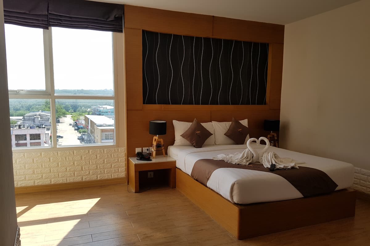 A hotel room with a large bed, a nightstand, a lamp, and a view of a parking lot and buildings.