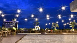 An outdoor dining area with string lights and tables, overlooking a cityscape at night. - The Vista Hotel (Sadao)